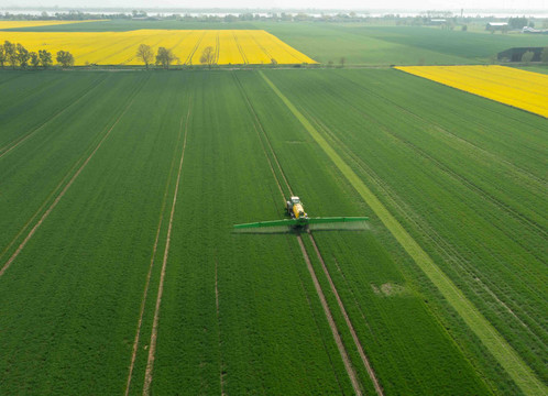 Aus der Luft ist ein Traktor auf landwirtschaftlich genutzten Flächen zu sehen, der Pflanzenschutzmittel versprüht