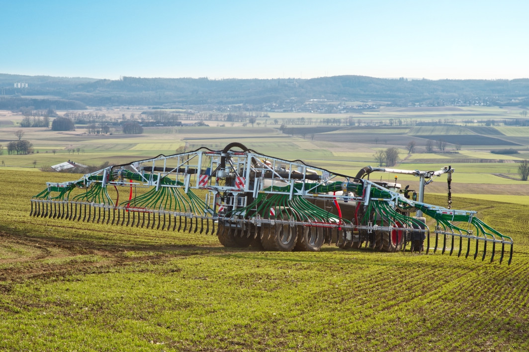 Traktor trägt Gülle mit einem Schleppschlauchsystem auf dem Feld aus.