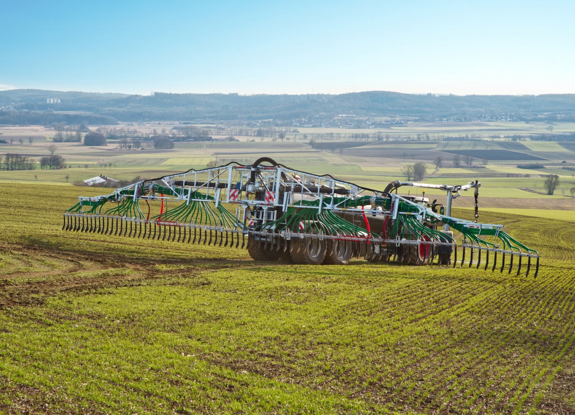 Traktor trägt Gülle mit einem Schleppschlauchsystem auf dem Feld aus.