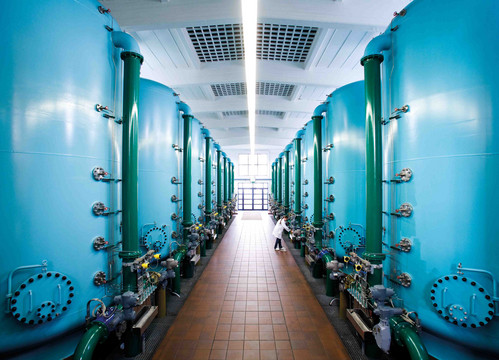 Links und rechts neben einem Gang stehen riesige, runde blaue Behälter, eine Frau überprüft einen davon.