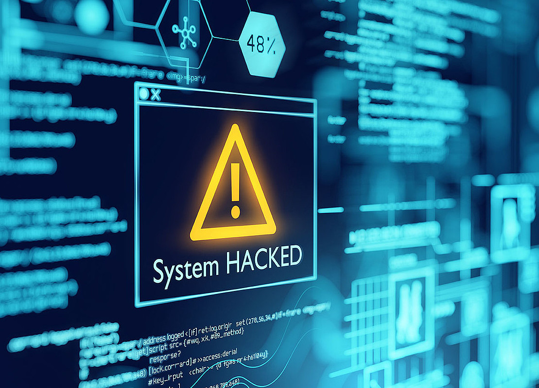 Auf einem Computerbildschirm steht ein großes dreieckiges Warnschild mit der Aufschrift "System hacked"