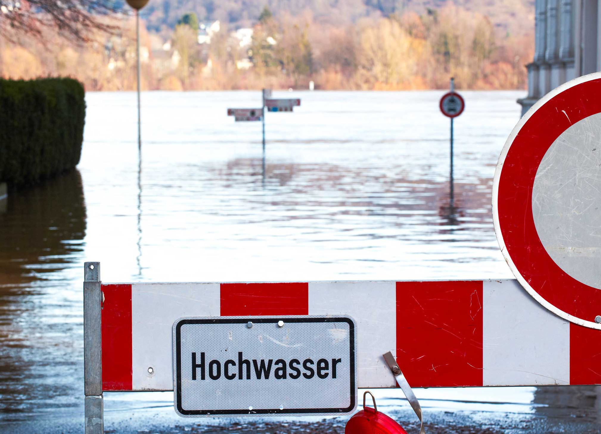 Überflutete Landschaft mit aus dem Wasser ragenden Verkehrsschildern und einer Sperre mit der Aufschrift "Hochwasser"