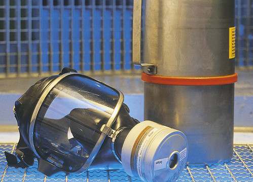 Eine Gasmaske liegt neben einer großen Flasche mit Odoriermittel