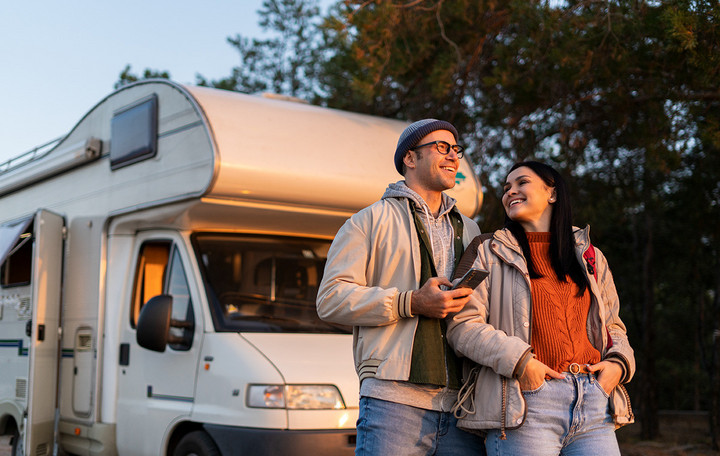Pärchen betrachten Sonnenuntergang, vor ihrem Camper stehend