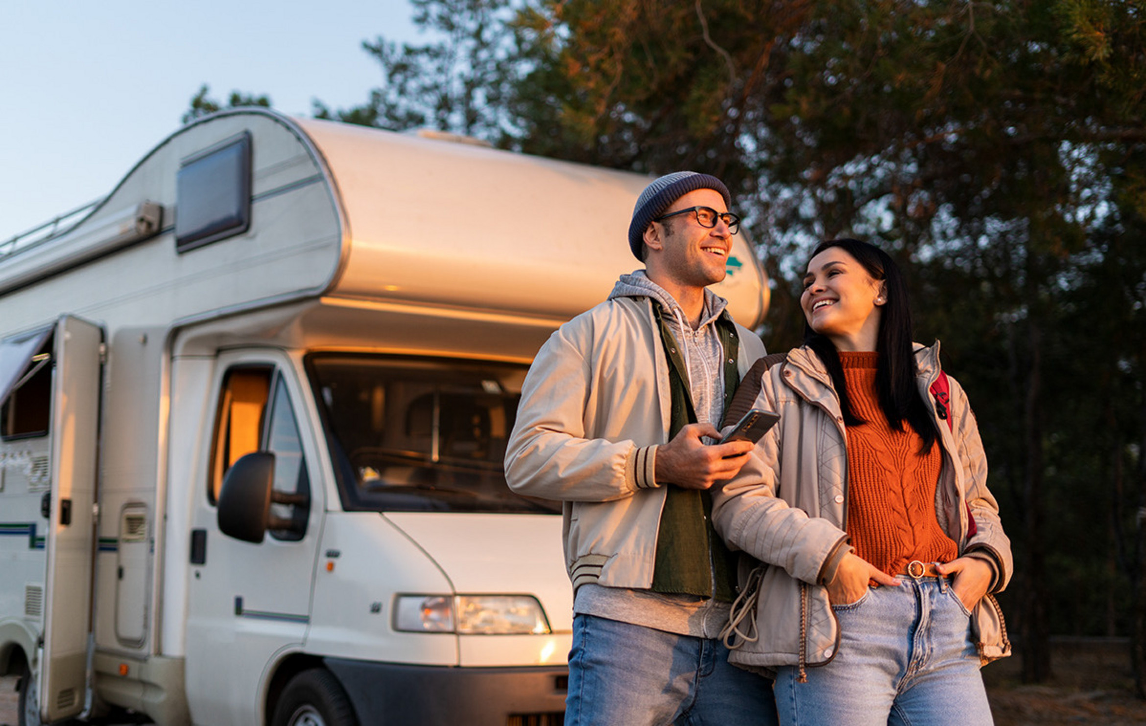Pärchen betrachten Sonnenuntergang, vor ihrem Camper stehend