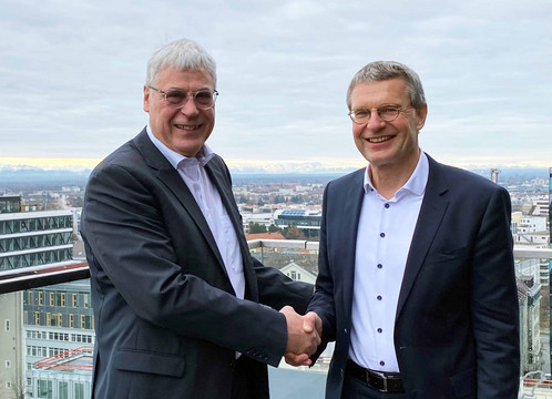 Die beiden Mänenr stehen auf einer Dachterrasse und schütteln sich die Hände