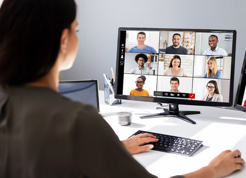 Junge Frau schaut auf zwei Bildschirme mit Teilnehmenden an einer Online-Konferenz