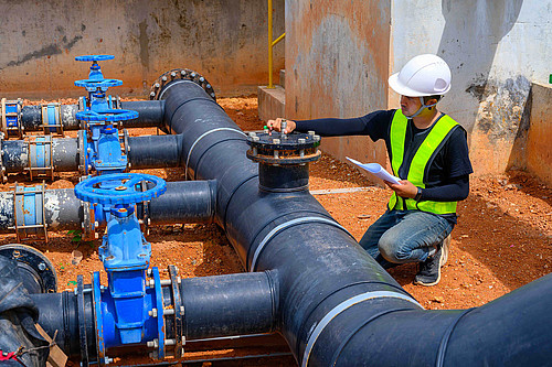 Ein Arbeiter überprüft in einer Baugrube eine Fernwasserleitung